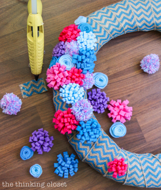 Securing the felt flowers and pom poms to the wreath using hot glue. Via thinkingcloset.com Securing the felt flowers and pom poms to the wreath using hot glue. Via thinkingcloset.com