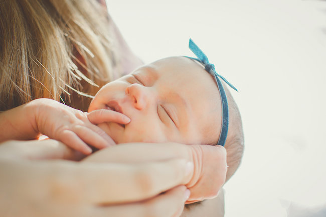 Juniper's 2 week newborn photography shoot: adorable hair bows, muslin swaddles, and a sweet smiling baby in a bucket. Brace yourself for the cuteness!